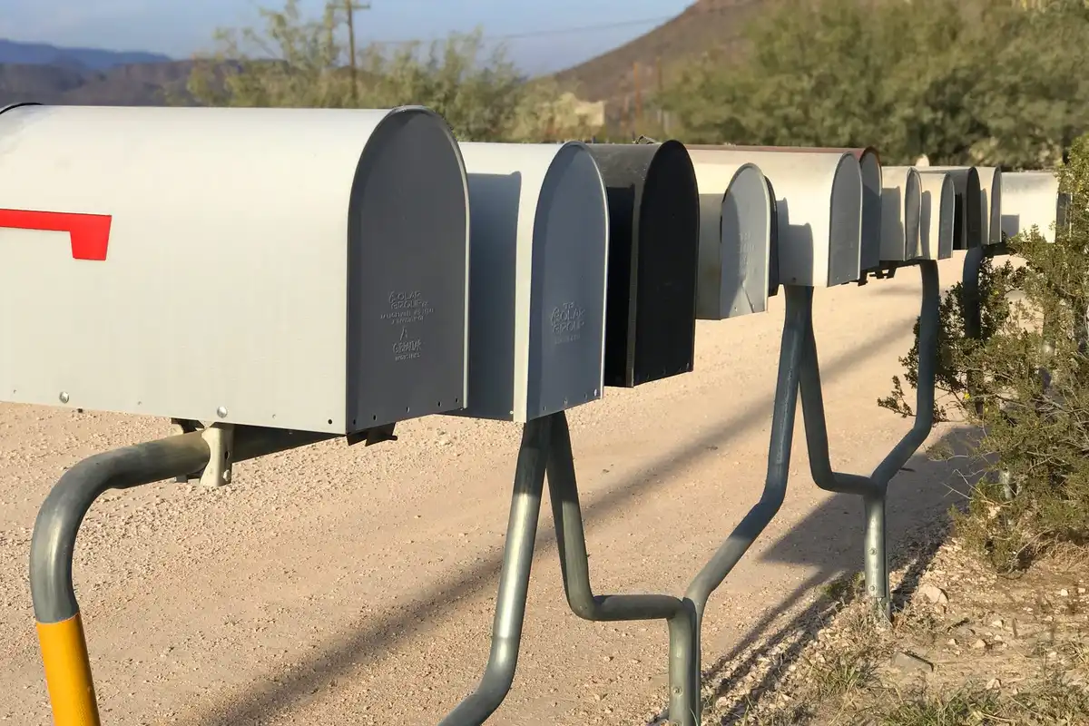 A long row of grey metal mailboxes on posts beside a gravel road.
