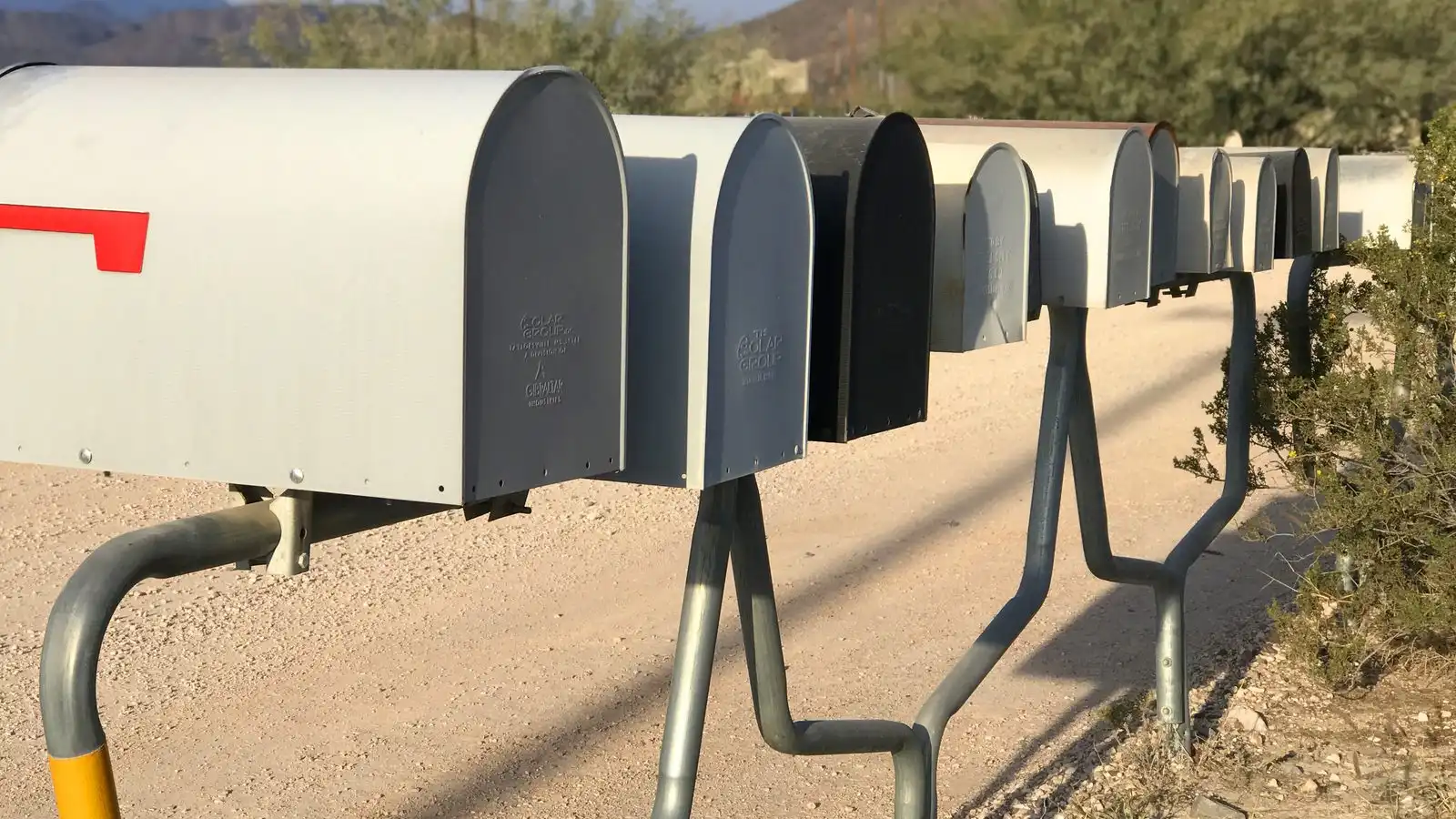 A long row of grey metal mailboxes on posts beside a gravel road.