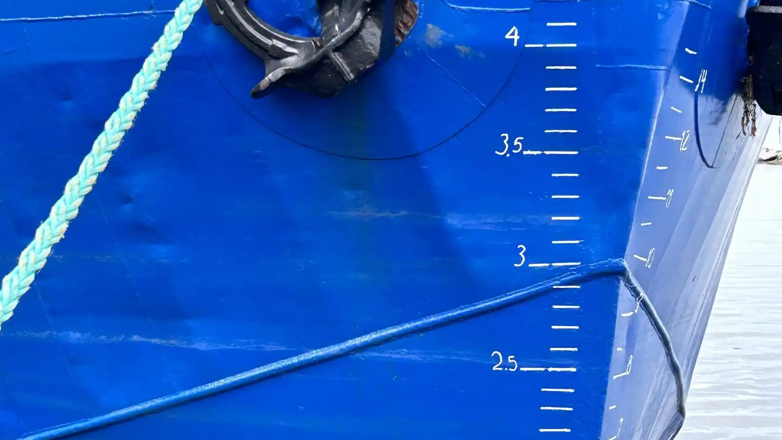 Draught marks painted in white on the bright blue hull of a ship, beside its anchor.