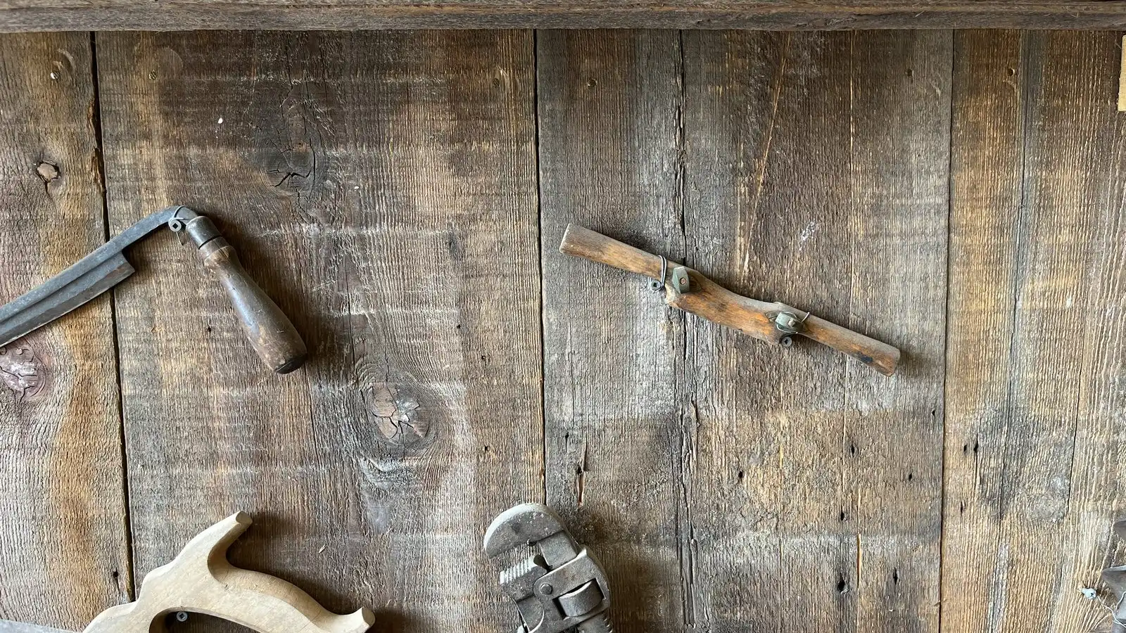 Old hand tools, a plane, a saw and a wrench, hung on a wall of weathered boards.