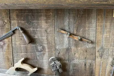 Old hand tools, a plane, a saw and a wrench, hung on a wall of weathered boards.