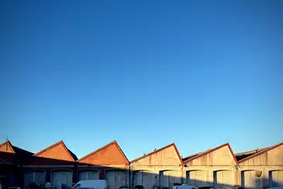 A row of brick warehouse roofs with sawtooth gables under a clear blue sky.