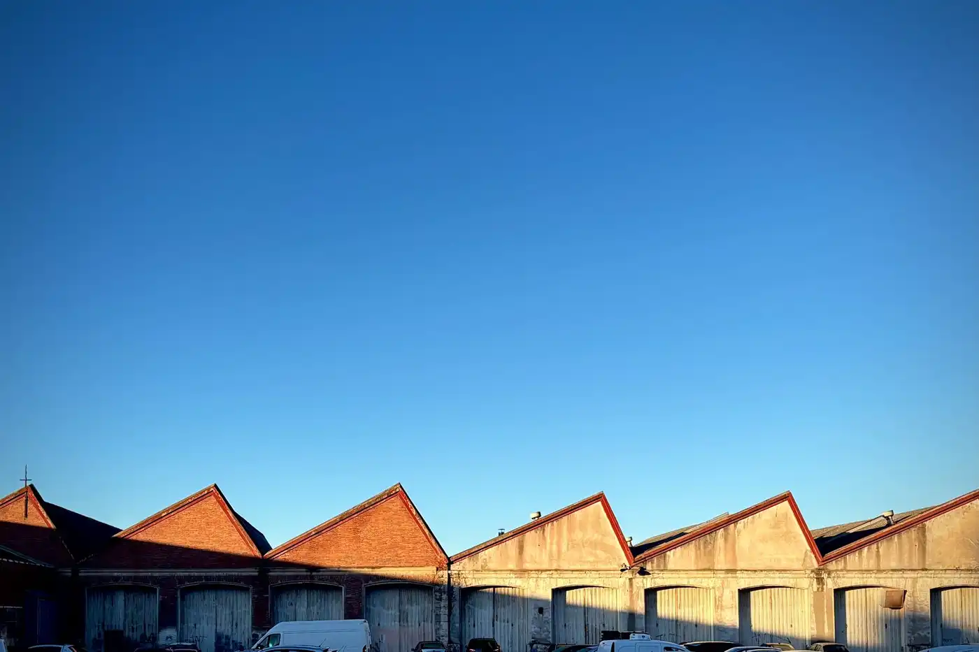 A row of brick warehouse roofs with sawtooth gables under a clear blue sky.
