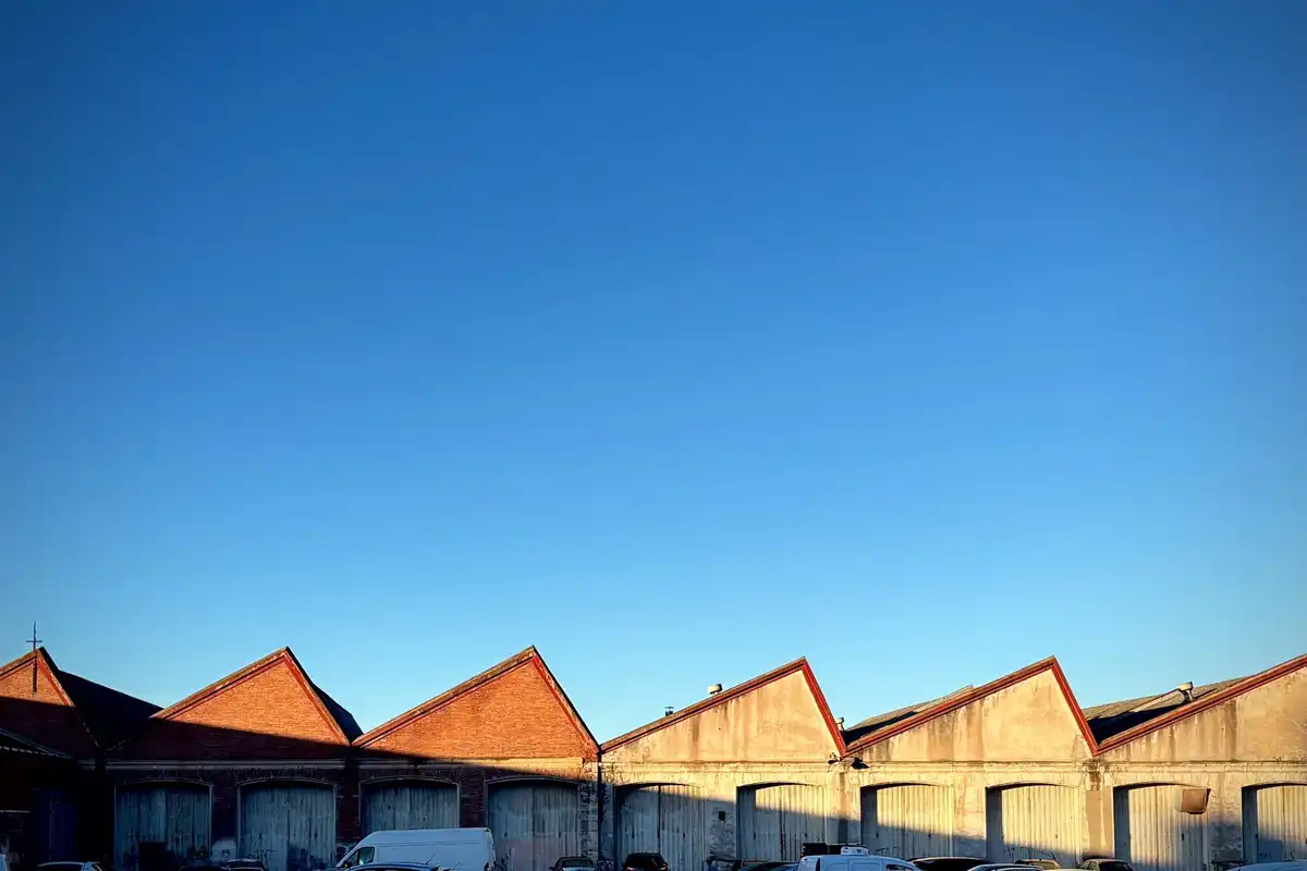A row of brick warehouse roofs with sawtooth gables under a clear blue sky.