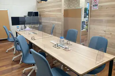 A shared work table with blue chairs, monitors and clear desk screens in a bright office.